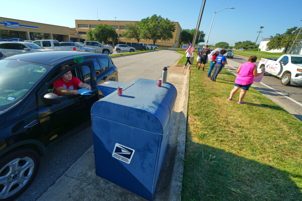 A person drops envelopes into a mailbox as postal workers participate in a national day of action outside a U.S. Post Office building, Tuesday, July 28, 2026, in Fort Worth, Texas. (AP Photo/Julio Cortez)