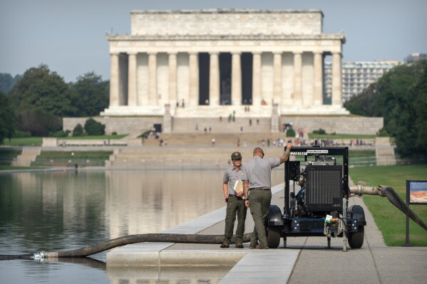 National Park Service workers stand near a pump placed next to the Lincoln Memorial Reflecting Pool, Friday, July 10, 2026, in Washington. (AP Photo/Mark Schiefelbein)