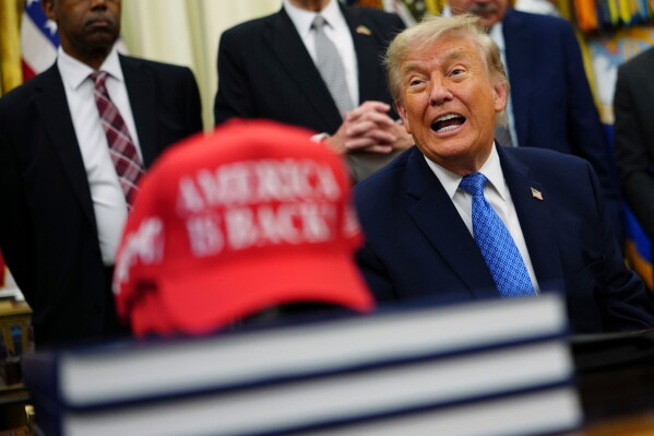 President Donald Trump speaks alongside a red cap stating "America Is Back!" in the Oval Office of the White House, Friday, June 26, 2026, in Washington. (AP Photo/Julia Demaree Nikhinson)