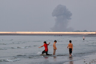 Tres niños juegan en el agua en el estrecho de Ormuz mientras al fondo se alza una columna de humo de una explosión, cerca de Bandar Abbas, Irán, el lunes 13 de julio de 2026. (Razieh Poudat/ISNA via AP)