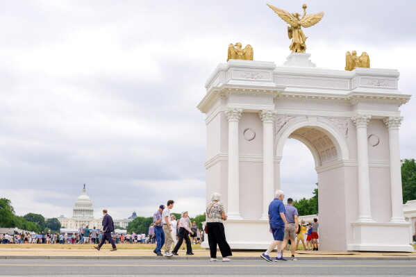 Visitors walk at the Great American State Fair with the triumphal arch model and the U.S. Capitol, in the background, Wednesday, July 8, 2026, in Washington. (AP Photo/Mariam Zuhaib)