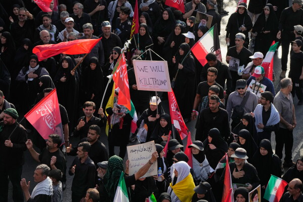 A mourner carries a sign reading "We Will Kill Trump" as people make their way to the funeral procession of the slain Iranian Supreme Leader Ayatollah Ali Khamenei in Tehran, Iran, Monday, July 6, 2026. (AP Photo/Vahid Salemi)